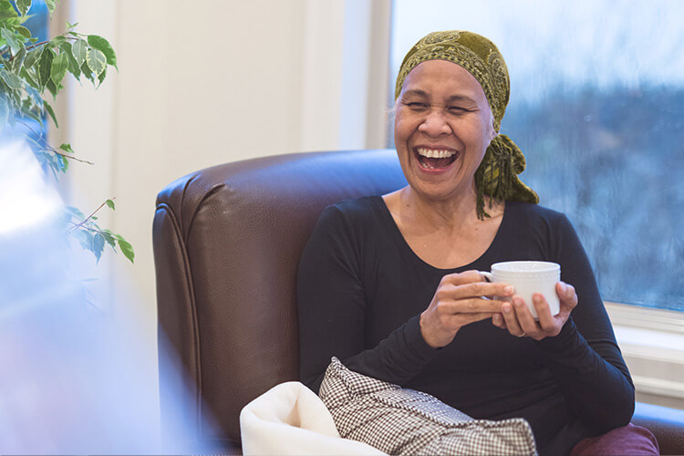 A woman with cancer laughing while enjoying a cup of tea