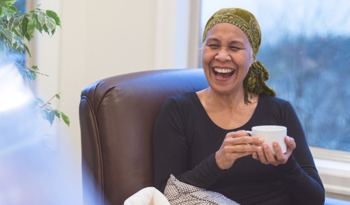A woman with cancer laughing while enjoying a cup of tea